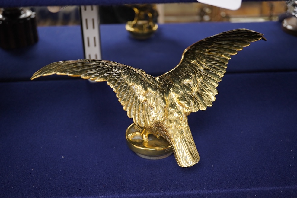 Two brass car mascots in the form of eagles, one mounted on a threaded radiator cap, the other mounted on a wooden base, the larger with a wingspan of 31cm. Condition - fair, one eagle with bent wing.